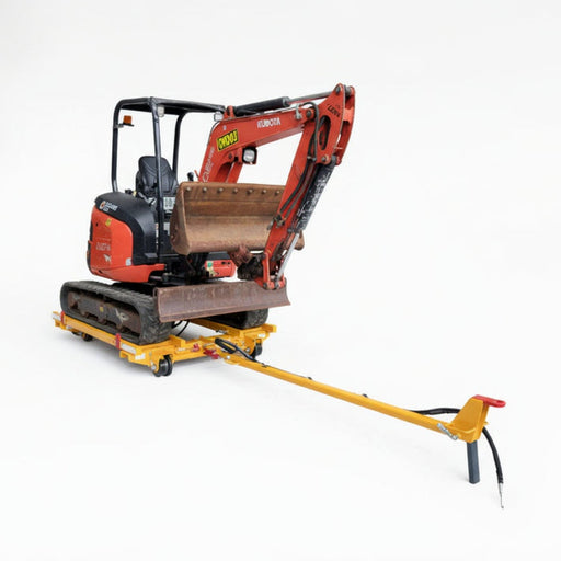 Small excavator on a rail troller trailer in an workshop with vehicles and equipment in the background.