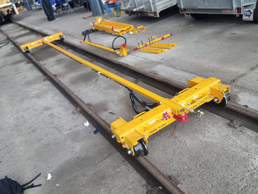 Yellow Rail and girder trolley on a concrete surface with other similar equipment in the background.
