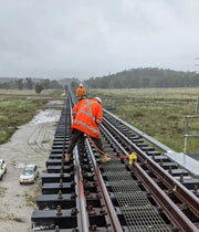 a rail worker on a bridge attached to a yellow harrybilt rail dog fall arrest anchor with a lanyard