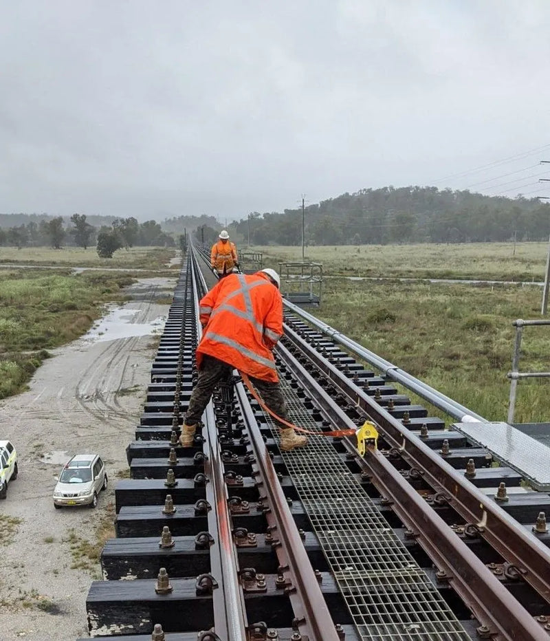 a rail worker on a bridge attached to a yellow harrybilt rail dog fall arrest anchor with a lanyard