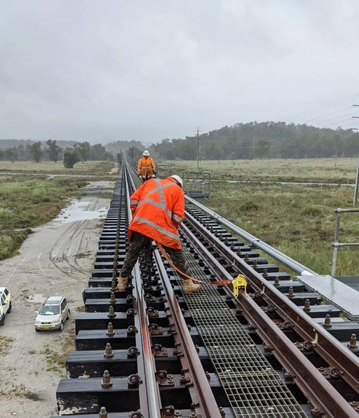 a worker on a bridge attached to a yellow harrybilt rail pup fall arrest anchor with a lanyard